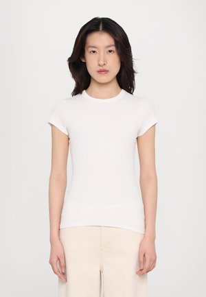 White, short-sleeve, fitted t-shirt made of ribbed fabric; features a round neckline and seamless shoulders. Worn with light-colored pants.