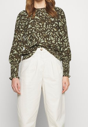 Blusa a maniche lunghe verde e nera con motivo, caratterizzata da polsini smock e una vestibilità rilassata, abbinata a pantaloni beige larghi.
