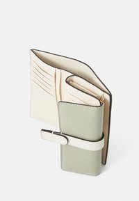 Portefeuille avec un intérieur crème comportant plusieurs emplacements pour cartes, un extérieur texturé vert clair et une fermeture à sangle blanche.