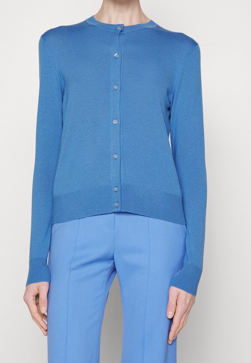 Blå, lättvikts långärmad cardigan med rund hals, knappstängning och ribbad nederkant. Stylad med matchande blå byxor.