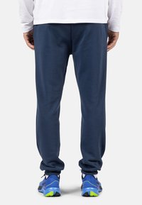 Marineblaue Jogginghosen mit weicher Textur, elastischem Bund und schmal zulaufenden Beinen. Kombiniert mit blauen und grünen Sportschuhen.