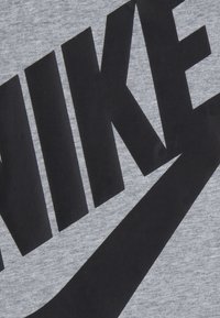 Šedé tričko s krátkým rukávem s velkým černým logem "NIKE" a designem swoosh. Měkká textura s hladkým povrchem.