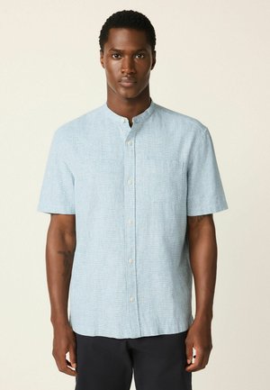 Hellblaues, kurzärmeliges Hemd mit Stehkragen, das aus einem dezenten, strukturierten Stoff gefertigt ist und eine einzelne Brusttasche aufweist.