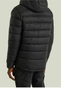 Sort pufferjakke med hætte, kviltet design og elastiske manchetter. Fremstillet af letvægtsmateriale med en glat, blank overflade.