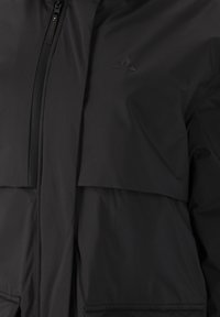 Svart puffjacka med dragkedja, utrustad med en fickdetalj med lock och en subtil logotyp på bröstet. Slät, texturerad tyg.