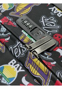 Lucchetto a combinazione con due cursori in metallo su una superficie di tessuto nero decorata con loghi colorati di squadre sportive.