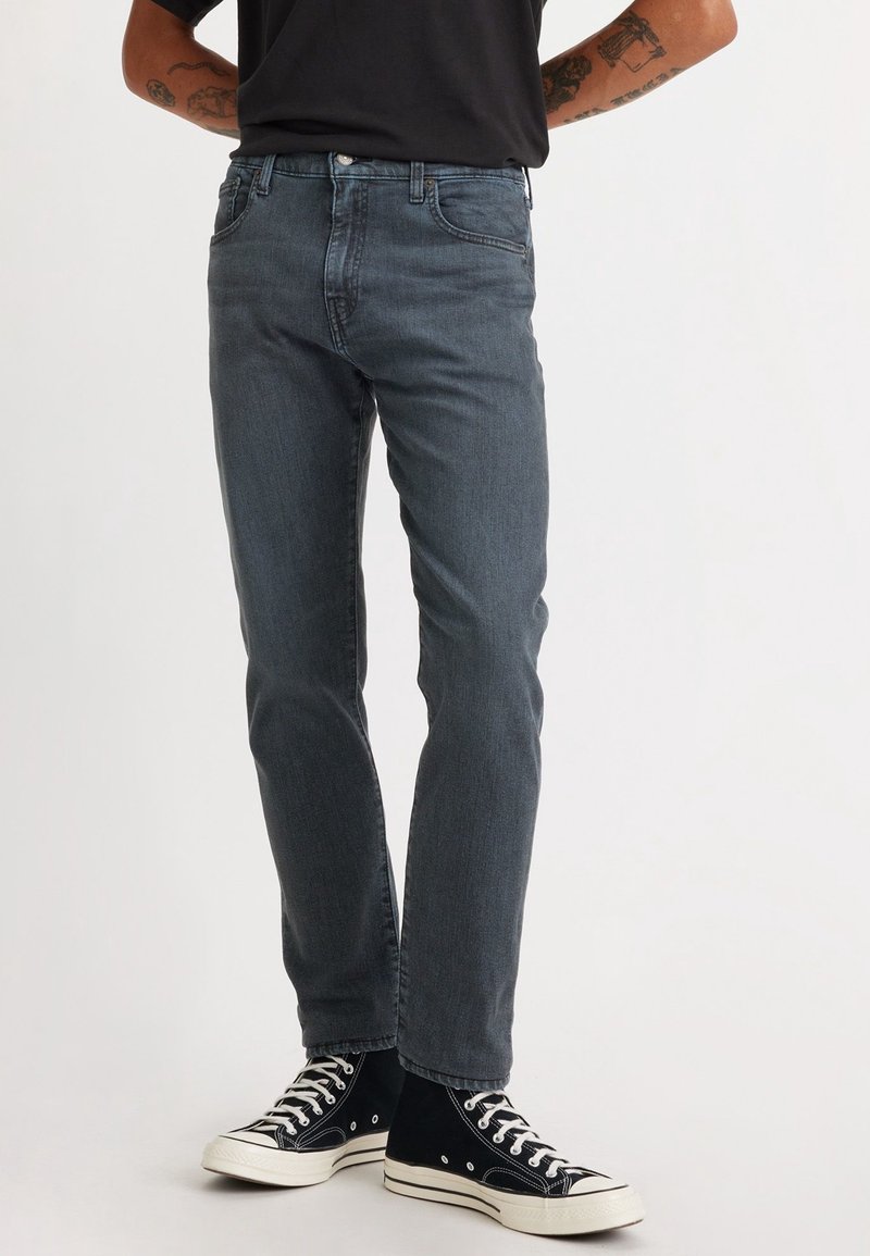 Slim-fit mörkgrå jeans med en klassisk femficksdesign, denimmaterial och subtila sömnadsdetaljer, kombinerat med svarta högkängor.