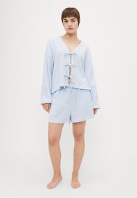 Lyseblå pysjamas-sæt med en langærmet top med dyb V-udskæring, frontknytningslukning og matchende shorts med elastisk talje.