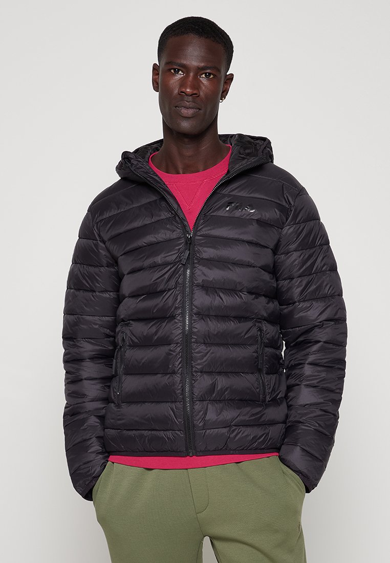 Giacca a vento nera con cappuccio, caratterizzata da un design trapuntato, chiusura con zip frontale e tasche laterali. Indossata sopra una maglietta rossa.