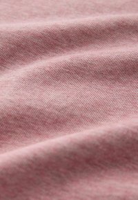 Gros plan sur un tissu rose doux et texturé avec un fin nervurage diagonal et des plis subtils créant des ombres délicates.