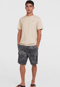Beige t-paita lyhyillä hihoilla, jossa on logo, yhdistettynä harmaisiin cargo-shortseihin, joissa on musta lehvämusteri. Yhdistetty tummiin flip-flop-kenkiin.