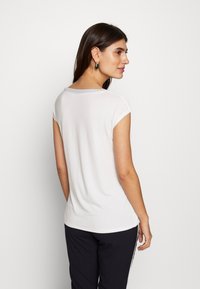 T-shirt blanc à manches courtes avec un col arrondi, en tissu doux, ourlet incurvé et silhouette ajustée, associé à un pantalon noir avec des rayures latérales.