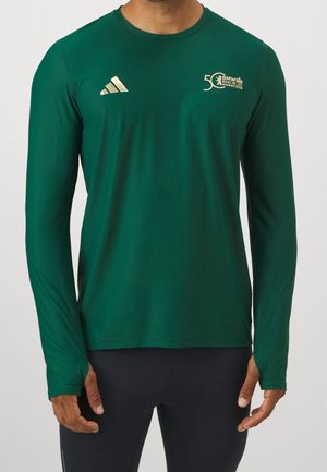 Homme portant un maillot de marathon vert à manches longues avec les logos dorés Adidas et BMW Berlin Marathon pour le 50e anniversaire sur la poitrine.