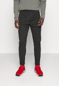 Svarta träningsbyxor med elastiskt midjeband, smal passform och mjukt material, ihop med klarröda sneakers.