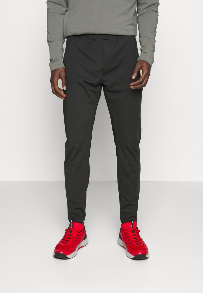 Svarta träningsbyxor med elastiskt midjeband, smal passform och mjukt material, ihop med klarröda sneakers.