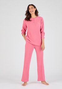 Conjunto de loungewear de color rosa con textura acanalada, que incluye mangas largas y un escote abotonado, combinado con pantalones de pierna recta. Textura suave y ajuste relajado.