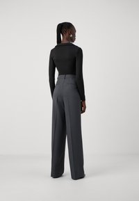 Haut noir à manches longues associé à un pantalon gris taille haute. Texture de tissu lisse avec un design ajusté et une silhouette cintrée.