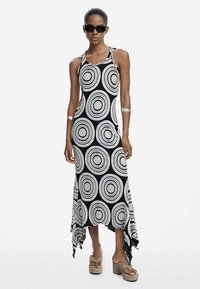 Juodos ir baltos spalvos apskritimų raštu su klostuotu kaklu, su asimetriška sukirpimo linija, pagaminta iš lengvos medžiagos, derinama su storais platformos batais.