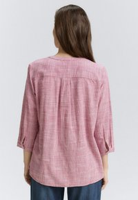 Chemise à carreaux rose avec manches trois-quarts, détail de pli au dos et pattes de roulage aux poignets ; tissu léger et texturé.
