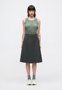 Haut sans manches texturé vert avec un design froncé, associé à une jupe trapèze gris foncé, porté avec des chaussettes grises et des baskets blanches.