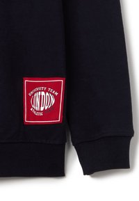 Sudadera marina con puños acanalados. Presenta un parche rectangular rojo con texto blanco: "UNIVERSITY TEAM LONDON ATHLETIC CREW."