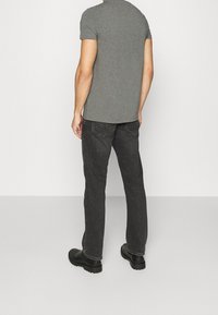 Grå tætsiddende t-shirt parret med sorte denim jeans. Jeansene har kontrastsyninger og et lige ben-design. Sorte sko fuldender looket.