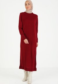 Vestido de punto rojo de manga larga con textura acanalada en el centro y puños ajustados, combinado con botas beiges hasta la rodilla.