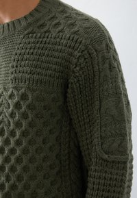 Mørkegrøn strikket sweater med teksturerede mønstre, herunder kabel- og honningkcomb, samt ribbet halsudskæring og sidedele.