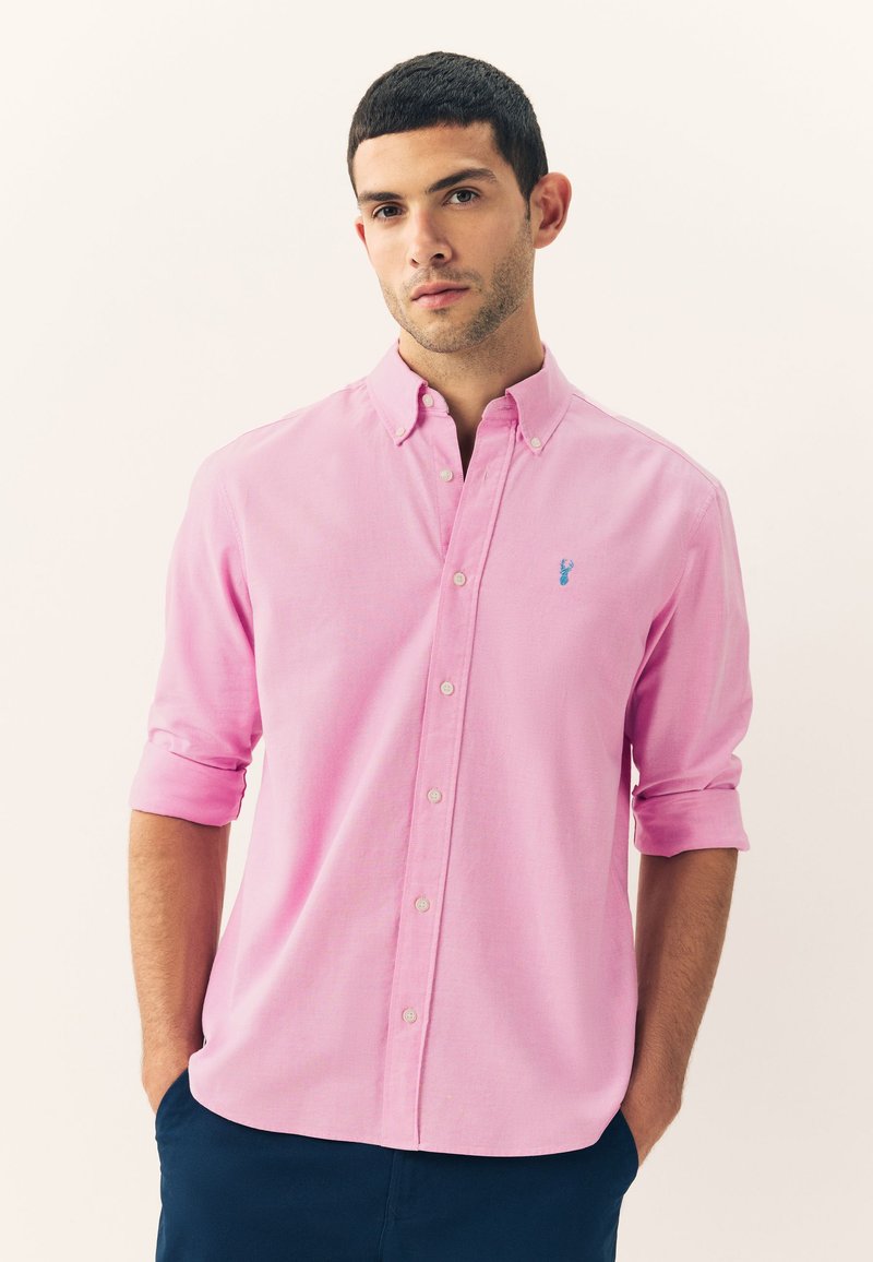 Light pink button-up shirt with rolled sleeves, featuring a small blue embroidered emblem on the left chest and a classic collar design.