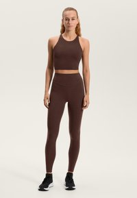 Barna sportos crop top és magas derekú leggings sima, rugalmas anyagból. Karcsú kialakítással, minimális varrással. Tartalmaz sportcipőt is.
