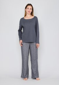 Grijze lange mouw top met een brede halslijn, gecombineerd met grijze broek met een geometrisch patroon. De stof lijkt zacht en lichtgewicht.