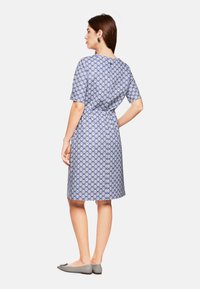 Kurzes, blaues Kleid mit gemustertem Design, tailliert, knielang und kombiniert mit grauen Ballerinas.