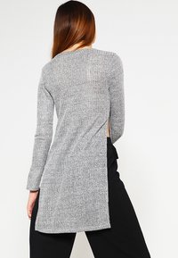Top a maniche lunghe grigio in maglia con un motivo testurizzato e un design con schiena aperta, che offre una vestibilità ampia e rilassata.