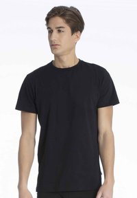 Sort bomulds t-shirt med korte ærmer, rund halsudskæring og et minimalistisk design, vist på en model mod en hvid baggrund.