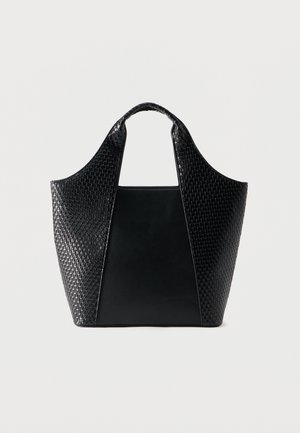 Sac fourre-tout noir avec des panneaux en cuir lisse et tissé, des poignées courtes et une base rectangulaire large, présenté sur un fond clair uni.