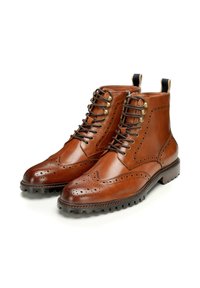 Stivali alla caviglia in pelle marrone con dettagli brogue, punta rotonda, suola in gomma nera e linguette laterali per indossarli facilmente. Lacci e occhielli in ottone.