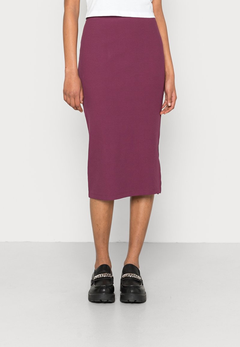 Aansluitend, geribbeld midi-rok in diep paars, gemaakt van rekbaar materiaal. Gecombineerd met zwarte loafers met een kettingaccent.