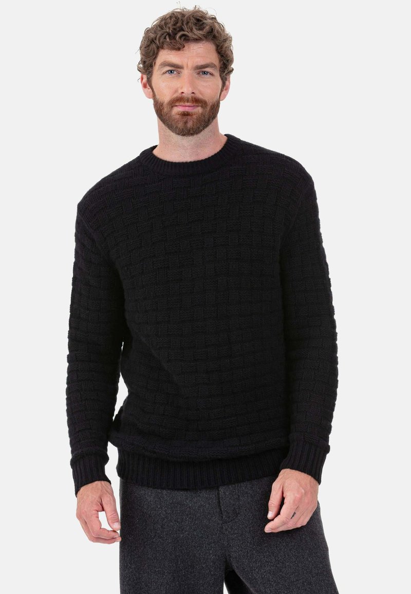 Schwarzer Strickpullover mit strukturierter Webart, rundem Ausschnitt sowie gerippten Bündchen und Saum. Kombiniert mit grauer Hose.