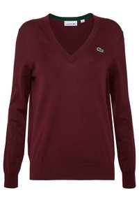 Vinröd V-ringad tröja med långa ärmar, gjord av mjukt tyg. Har en grön krage och en liten broderad logotyp på vänster bröst.