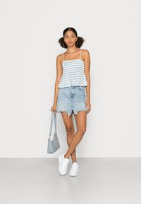 Top peplum listrado em azul e branco com alças finas, combinado com uma saia de denim clara com bainha desfiada. Ténis brancos e uma carteira azul clara completam o visual.