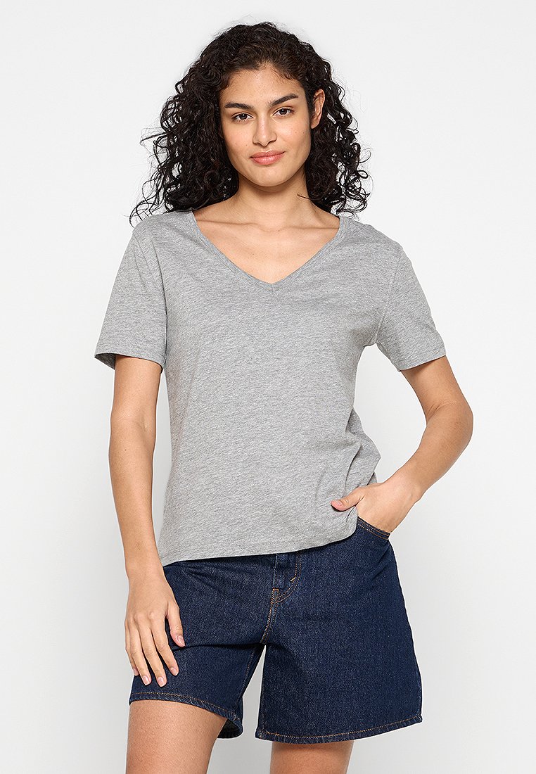 Graues Baumwoll-T-Shirt mit V-Ausschnitt und kurzen Ärmeln, das einen lockeren Schnitt und eine glatte Textur aufweist. Getragen mit blauen Jeansshorts.