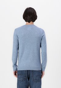 Ljusblå crewneck-tröja i mjukt stickat material, med långa ärmar och ribbade muddar. Bärs med mörkblå denimjeans.