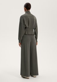 Temno siva, sproščena trenirka z ovratnikom, vključujoča pas s pasom in široke hlače. Mehka tkanina z minimalnimi detajli.