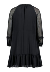 Schwarz Kleid mit langen, durchsichtigen Ärmeln, gerafftem Ausschnitt und Rüschensaum. Hergestellt aus leichtem Stoff, hat es eine lockere Passform und geknöpfte Manschetten.