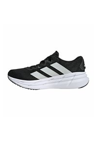 Zwarte sport schoenen met een gestructureerde stoffen bovenkant, voorzien van drie witte strepen, een gewatteerde witte zool en een zwarte buitenzool voor grip.