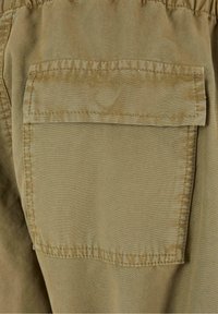 Khaki látka s hladkou strukturou, která má obdélníkovou nášivku. Nášivka má prošívané okraje a je umístěna na zadní straně oděvu.