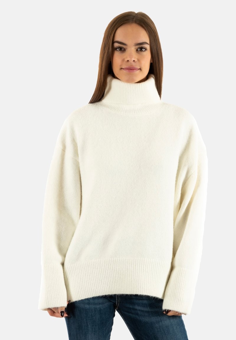 Maglione a collo alto bianco in morbido tessuto testurizzato con vestibilità oversize, maniche ampie e orlo a costine. Abbinato a jeans blu scuro.