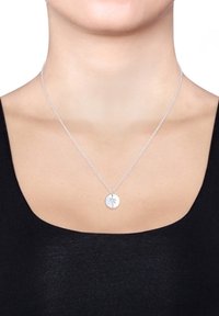 Silverhalsband med en cirkulär berlock som har en palmträdsdesign, hängande från en delikat kedja, visad mot en svart topp.