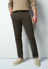 Donkere bruine, gemêleerde chino's met een smalle pasvorm, voorzien van een knoopsluiting en zijzakken, gecombineerd met licht beige sneakers.