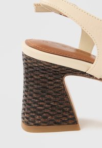 Μπεζ σανδάλι με ψηλό τακούνι, καφέ επενδεδυμένη ανατομική σόλα και πλεκτό, σκούρο καφέ τακούνι σε λευκό φόντο.